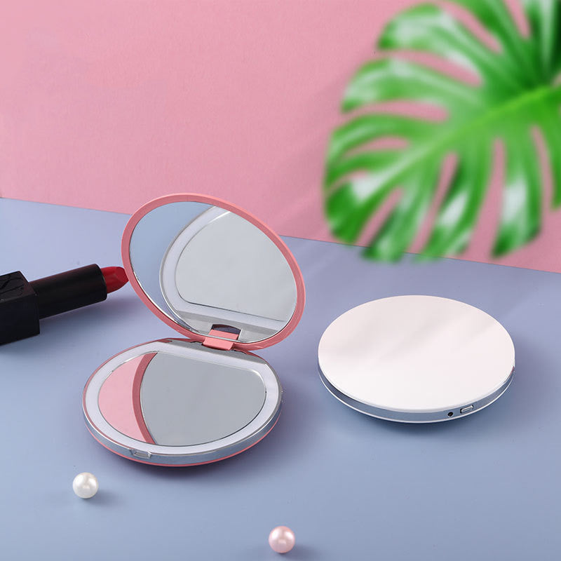 Two portable, round LED makeup mirrors in pink and white, set against a pink-and-blue background with a leaf.