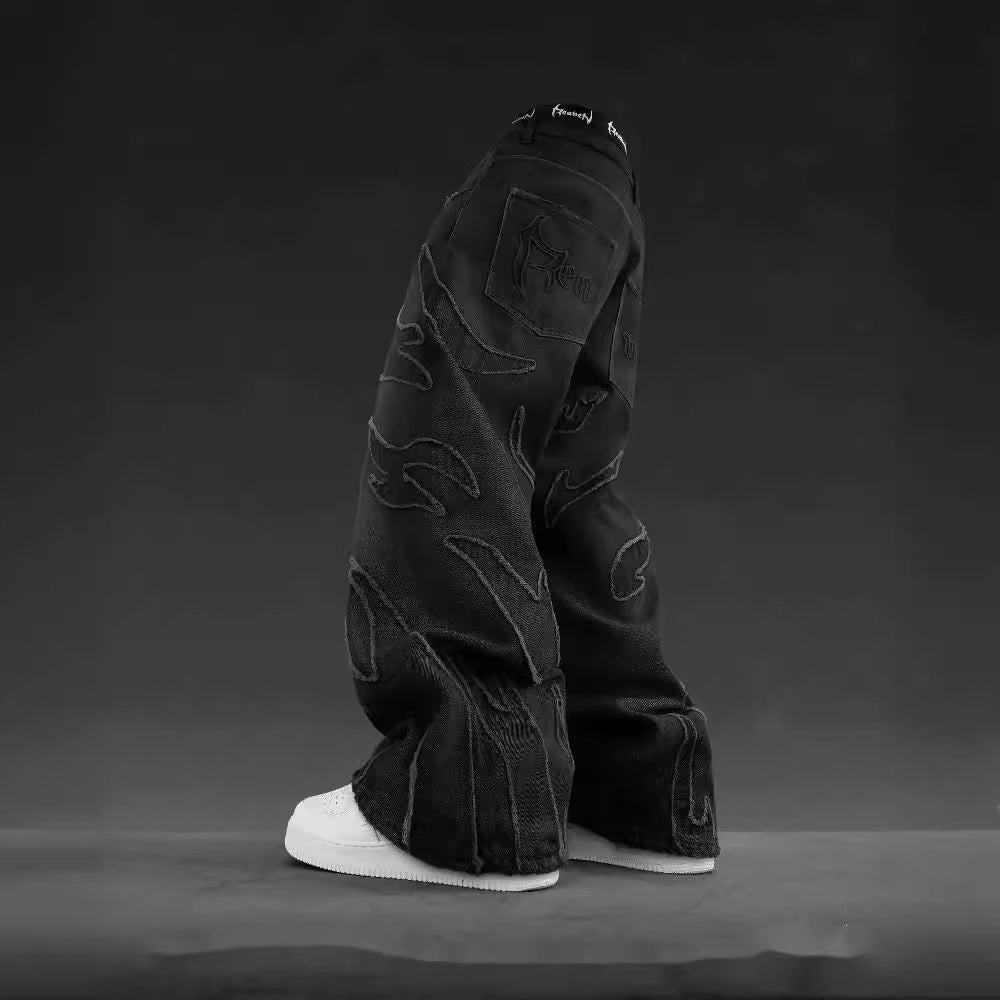 Black denim baggy hip-hop jeans featuring tonal flame patchwork, distressed detailing, and rear branded embroidery.