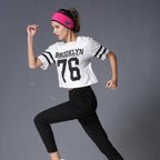 A woman running in a bright pink fabric Bluetooth headband, white athletic jersey, and black pants.