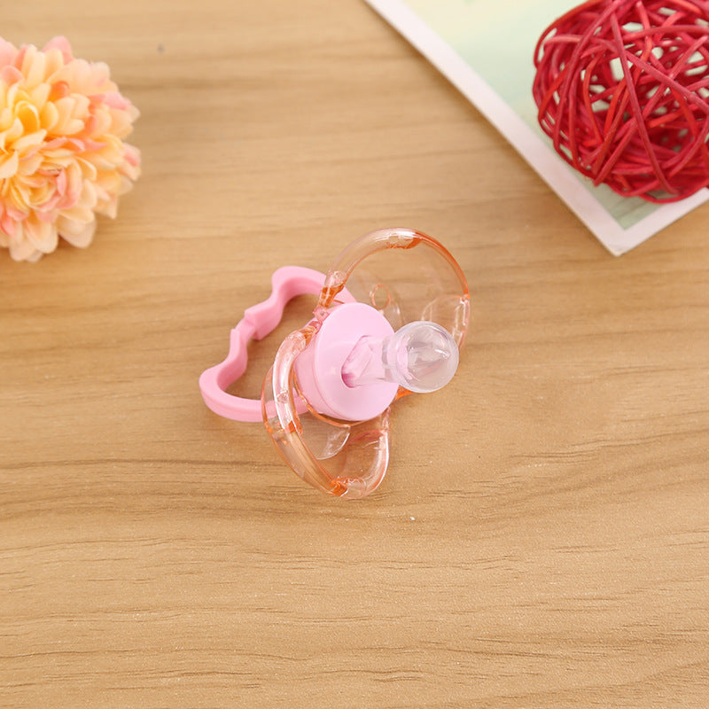 Pink translucent baby pacifier with a round silicone nipple on a wooden surface with decorative accents.