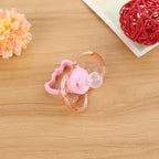 Pink translucent baby pacifier with a round silicone nipple on a wooden surface with decorative accents.