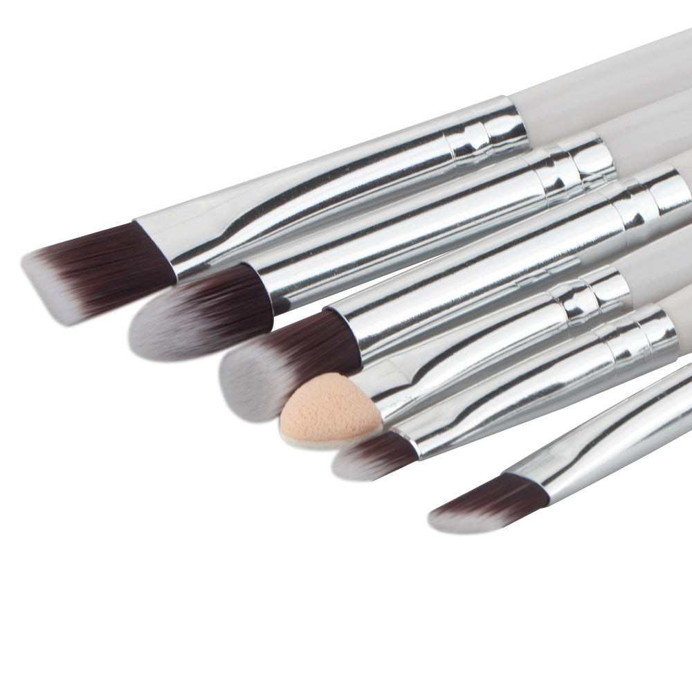 Six eye makeup brushes with white handles, silver ferrules, brown bristles, and one beige foam applicator tip.