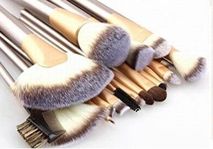 A set of 24 makeup brushes with gold handles and white-tipped bristles arranged on a white background.