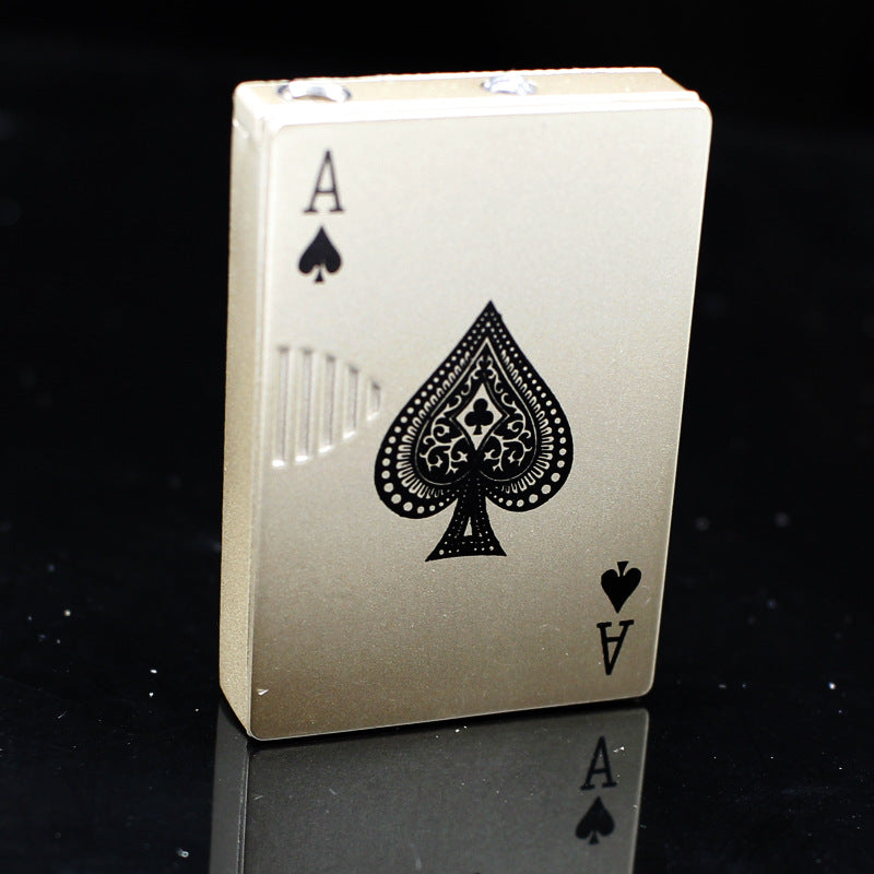 Gold metal playing card-style lighter, Ace of Spades design with detailed black engraving, standing on black surface.
