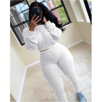 A woman wearing a white ribbed two-piece leisure set featuring a long-sleeve crop top and high-waisted leggings.