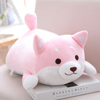 Soft, pink, plush Shiba Inu dog pillow with white belly, brown eyes, and a small curled tail, resting on a book.