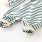 Baby jumpsuit with white and sage green stripes, ribbed cream cuffs, and snap buttons along the inner legs.