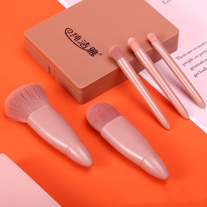 Five-piece rose-gold makeup brush set with soft pink bristles and a matching rectangular plastic storage case.
