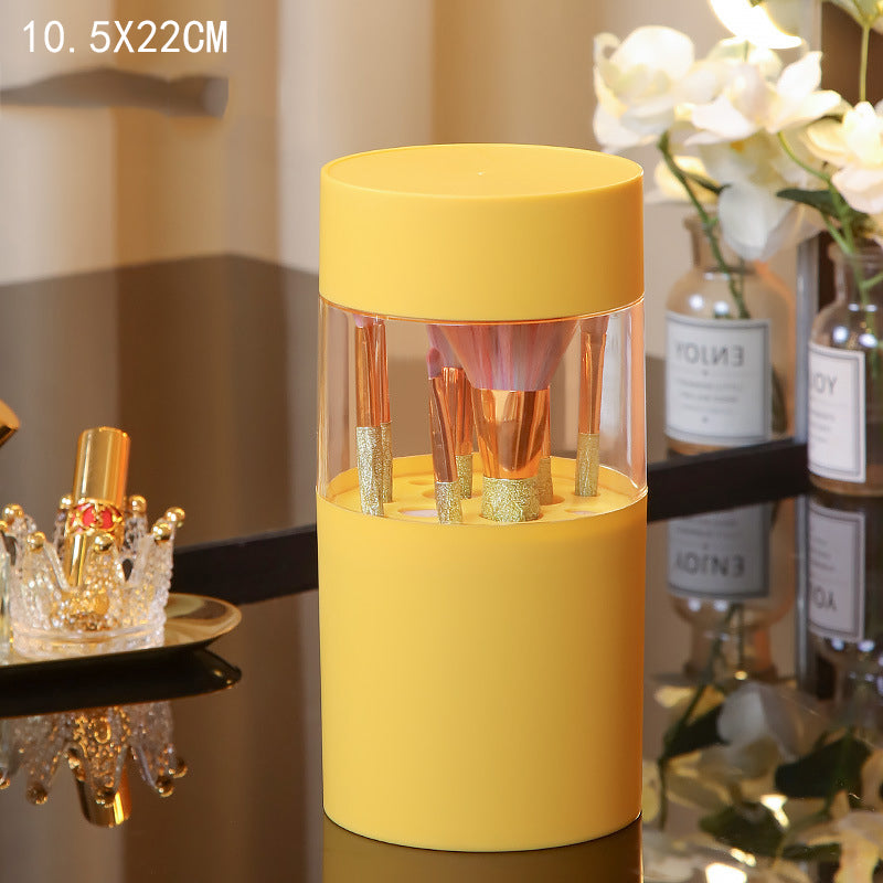 Yellow cylindrical plastic makeup brush organizer with a transparent middle section, holding various makeup brushes.
