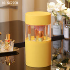 Yellow cylindrical plastic makeup brush organizer with a transparent middle section, holding various makeup brushes.