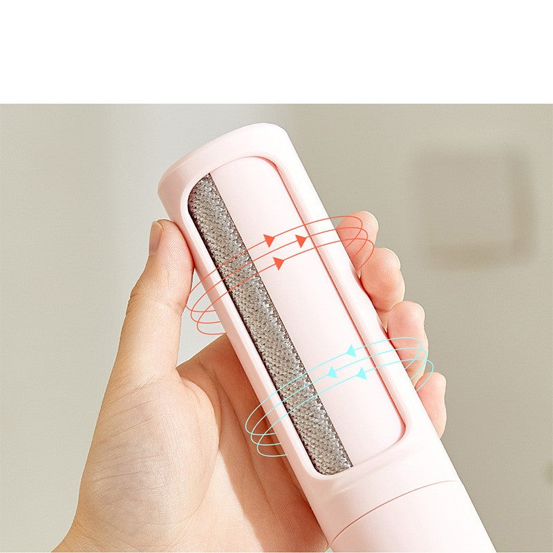 A hand holds a portable, light pink pet hair remover with a textured gray cleaning fabric surface.
