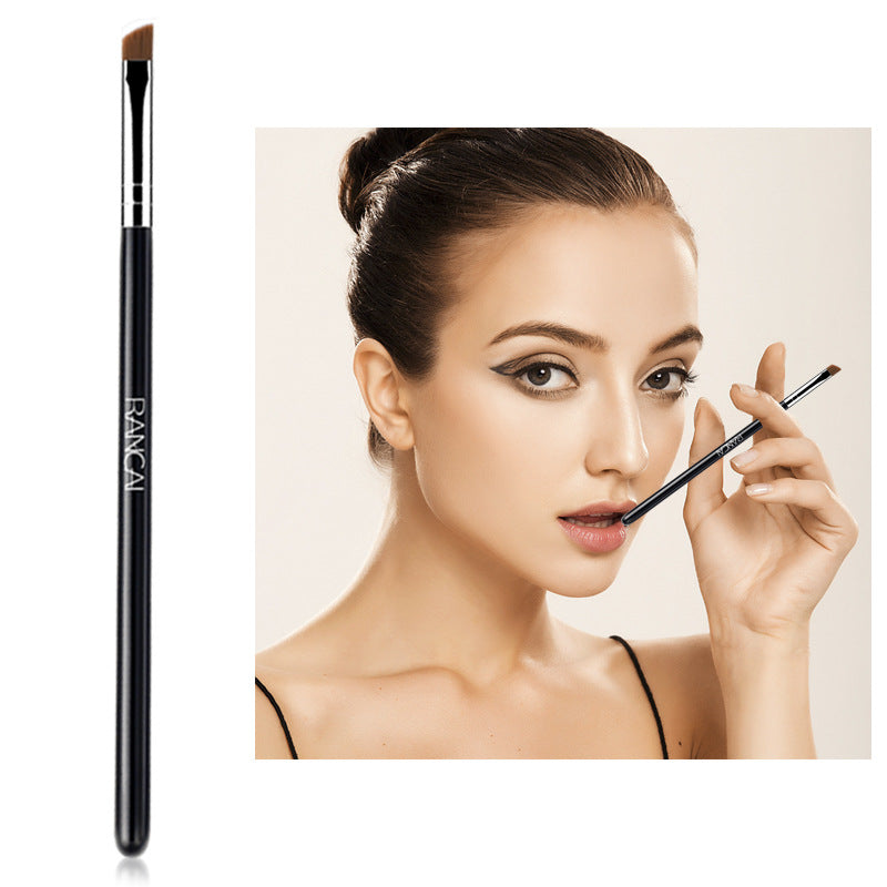 Angled eyebrow brush with a sleek black handle, silver ferrule, and brown bristles held by a model.