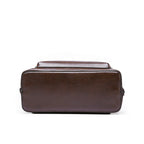 Bottom view of a rectangular, dark brown, textured leather-look structured bag with side zippers on a white background.