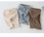 Three pairs of ribbed baby leggings in cream, blue, and brown, featuring elastic waists and decorative front buttons.