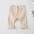 Beige ribbed baby leggings with an elastic waistband and decorative wooden button, featuring cuffed ankles.