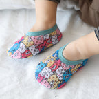 Baby wearing breathable, multicolor mesh first-step shoes with a cute bear pattern and teal elastic cuffs.