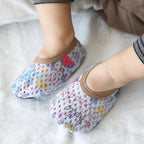 Baby wearing breathable white mesh first-step shoes with colorful summer prints and brown trim on a white surface.