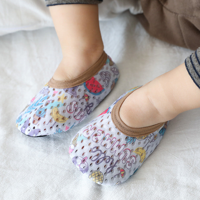 Baby wearing breathable white mesh first-step shoes with colorful summer prints and brown trim on a white surface.