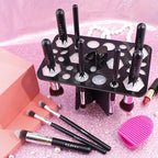Black 14-hole makeup brush drying rack with silicone inserts, holding Beakey brushes on a sparkly pink surface.