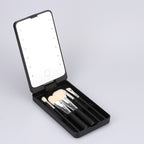 Black foldable makeup mirror with LED ring light and a set of four soft-bristled brushes in a compact storage case.