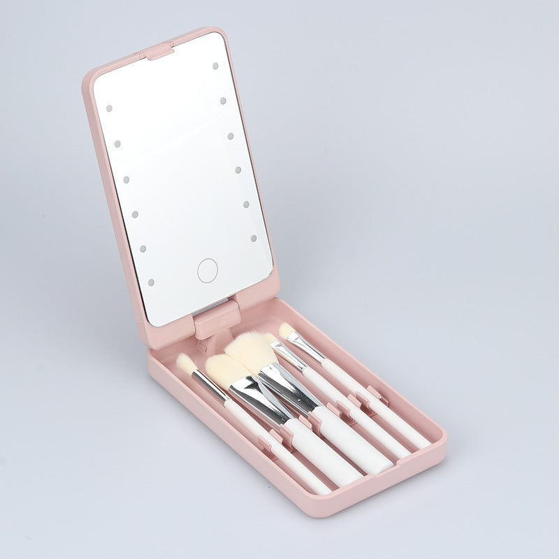 Pink folding makeup mirror with built-in LED lights and a set of four white brushes inside a compact case.