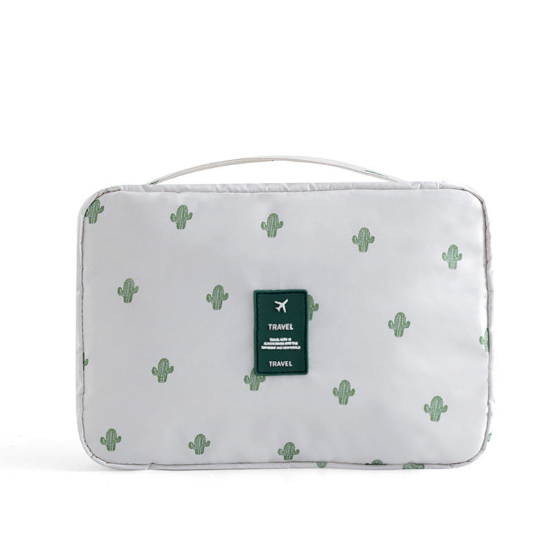 White travel cosmetic bag with green cactus print, top handle, and a green "Travel" logo patch on the front.