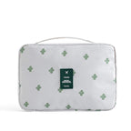 White travel cosmetic bag with green cactus print, top handle, and a green "Travel" logo patch on the front.