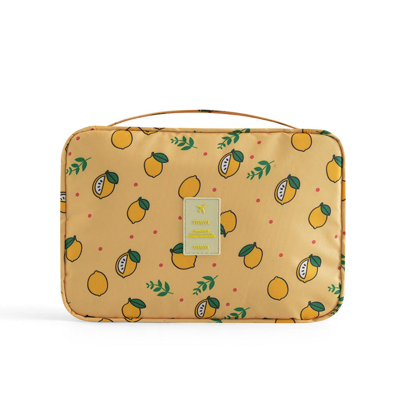 Yellow travel makeup bag featuring a lemon print, carrying handle, and a central "TRAVEL" logo patch on a white back.