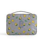 Gray travel cosmetic bag with a yellow lemon print, top handle, and central "TRAVEL" logo patch.