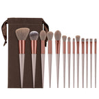 A 13-piece makeup brush set with soft fiber bristles, copper ferrules, beige handles, and a brown velvet storage pouch.