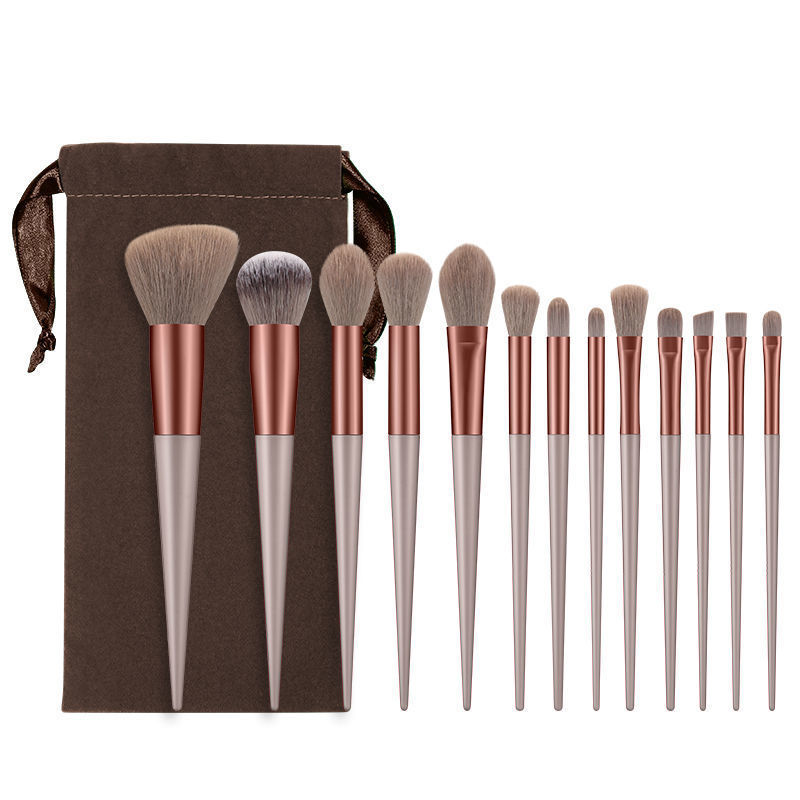 A 13-piece makeup brush set with soft fiber bristles, copper ferrules, beige handles, and a brown velvet storage pouch.