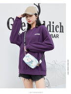 Woman wearing a purple sweatshirt and a holographic "LITTLE BEAUTY" crossbody bag with a branded black strap.