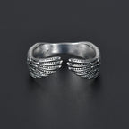 Antique silver open ring featuring detailed feathered angel wings on a dark background.
