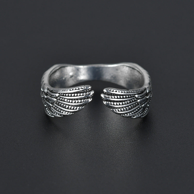 Antique silver open ring featuring detailed feathered angel wings on a dark background.