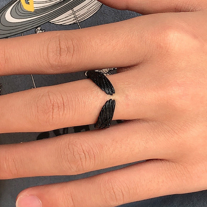 Matte black, open-style ring featuring detailed textured angel wings wrapped around a finger.