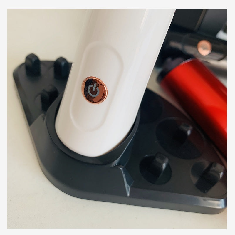 White electric makeup brush cleaner with a rose gold power button, resting in a black plastic storage base.