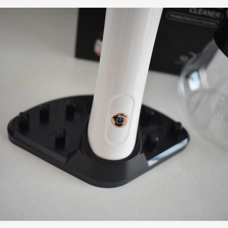White electric makeup brush cleaner with rose gold power button, standing on a black multi-slot storage base.