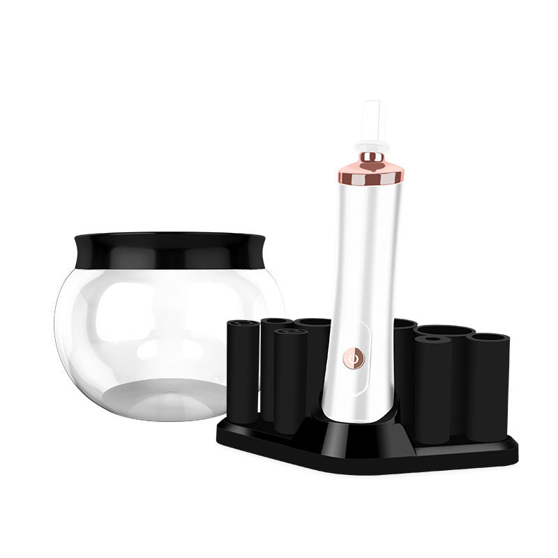 White and rose gold electric makeup brush cleaner with black base, storage stand, and clear glass cleaning bowl.