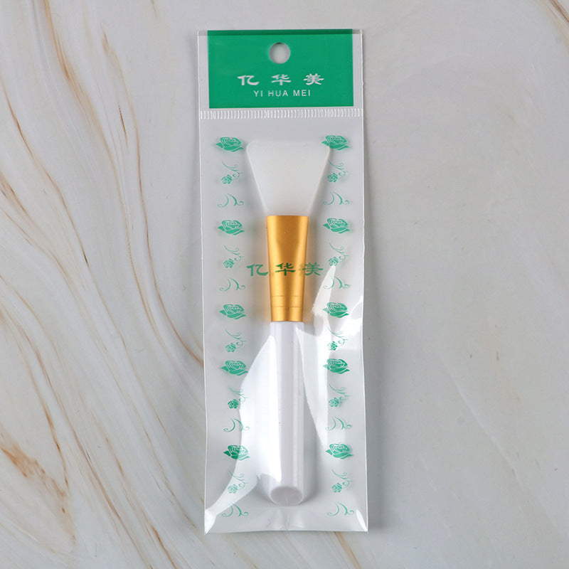 Silicone mask brush in clear retail packaging with a white handle, gold ferrule, and flexible white silicone head.