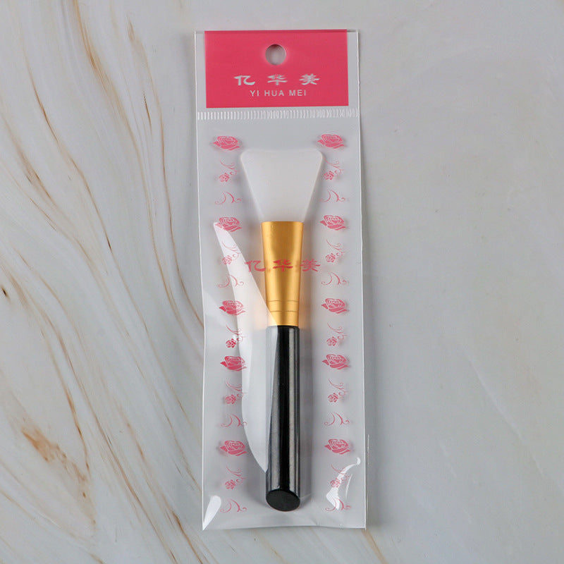 Silicone mask brush in a rose-patterned plastic sleeve, featuring a white head, gold ferrule, and black handle.