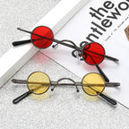 Two pairs of retro sunglasses with thin, dark metal frames, round red and yellow lenses on a glittery surface.