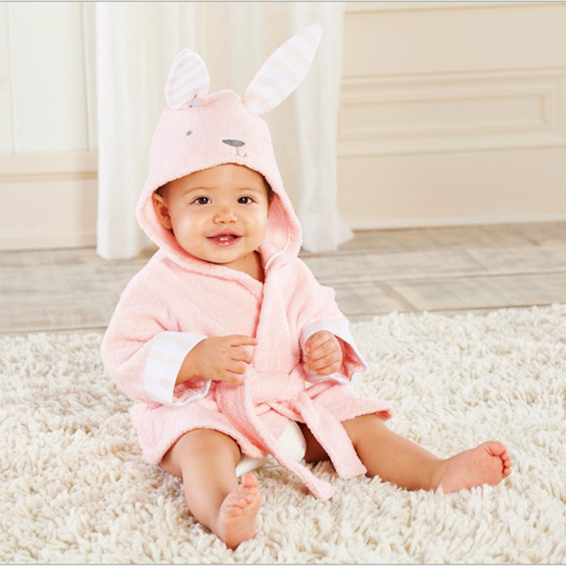 Baby wearing a soft, pink cotton hooded bathrobe with cute rabbit ears, sitting on a white shag rug.