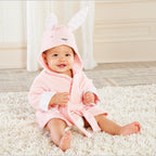 Baby wearing a soft, pink cotton hooded bathrobe with cute rabbit ears, sitting on a white shag rug.
