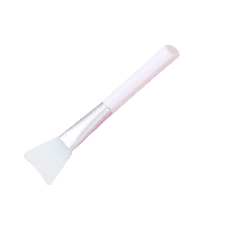 A silicone face mask brush with a white handle, silver ferrule, and flexible, translucent white silicone head.