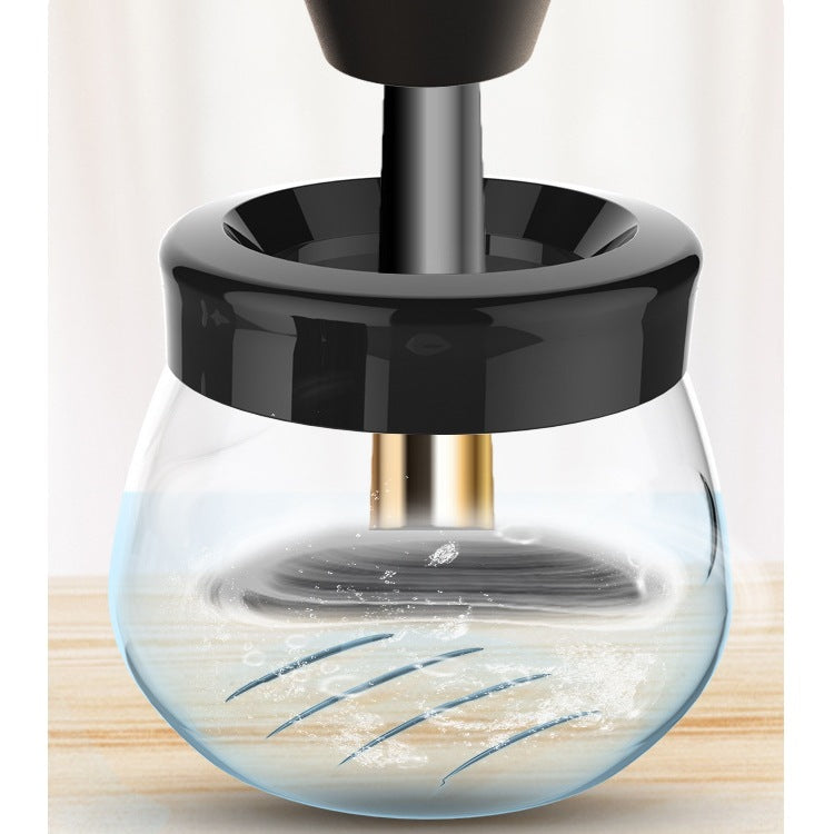 Electric makeup brush cleaner with black lid and clear glass bowl, featuring a central device cleaning a brush.