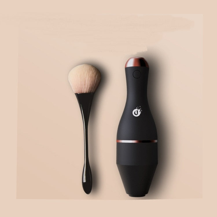 Matte black electric makeup brush cleaner with rose gold accents and a matching black brush on a beige background.