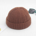 A brown, ribbed, cuffed knit beanie with a retro, hip-hop style design, positioned next to dark sunglasses.