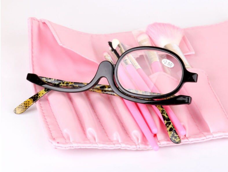 Black-frame makeup reading glasses with leopard print arms, placed on a pink makeup brush roll.
