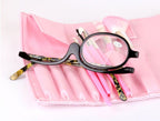 Black-frame makeup reading glasses with leopard print arms, placed on a pink makeup brush roll.
