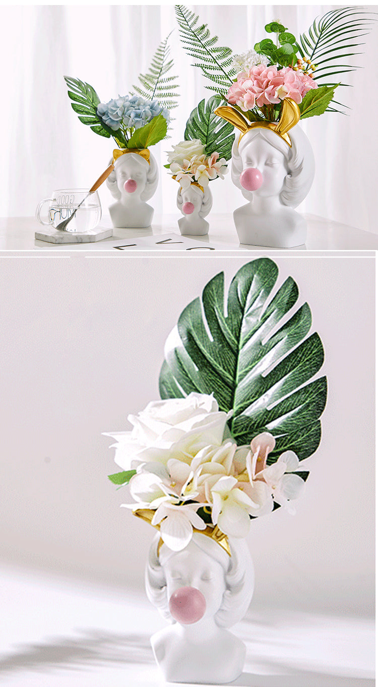 White resin girl-head vases featuring gold headbands and pink bubblegum spheres, filled with artificial flower bouquets.